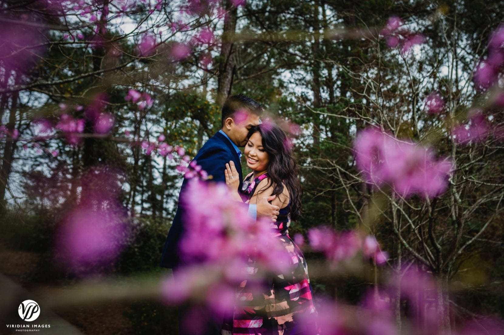 couple hugging through flowering trees in stone mountain park engagement photo