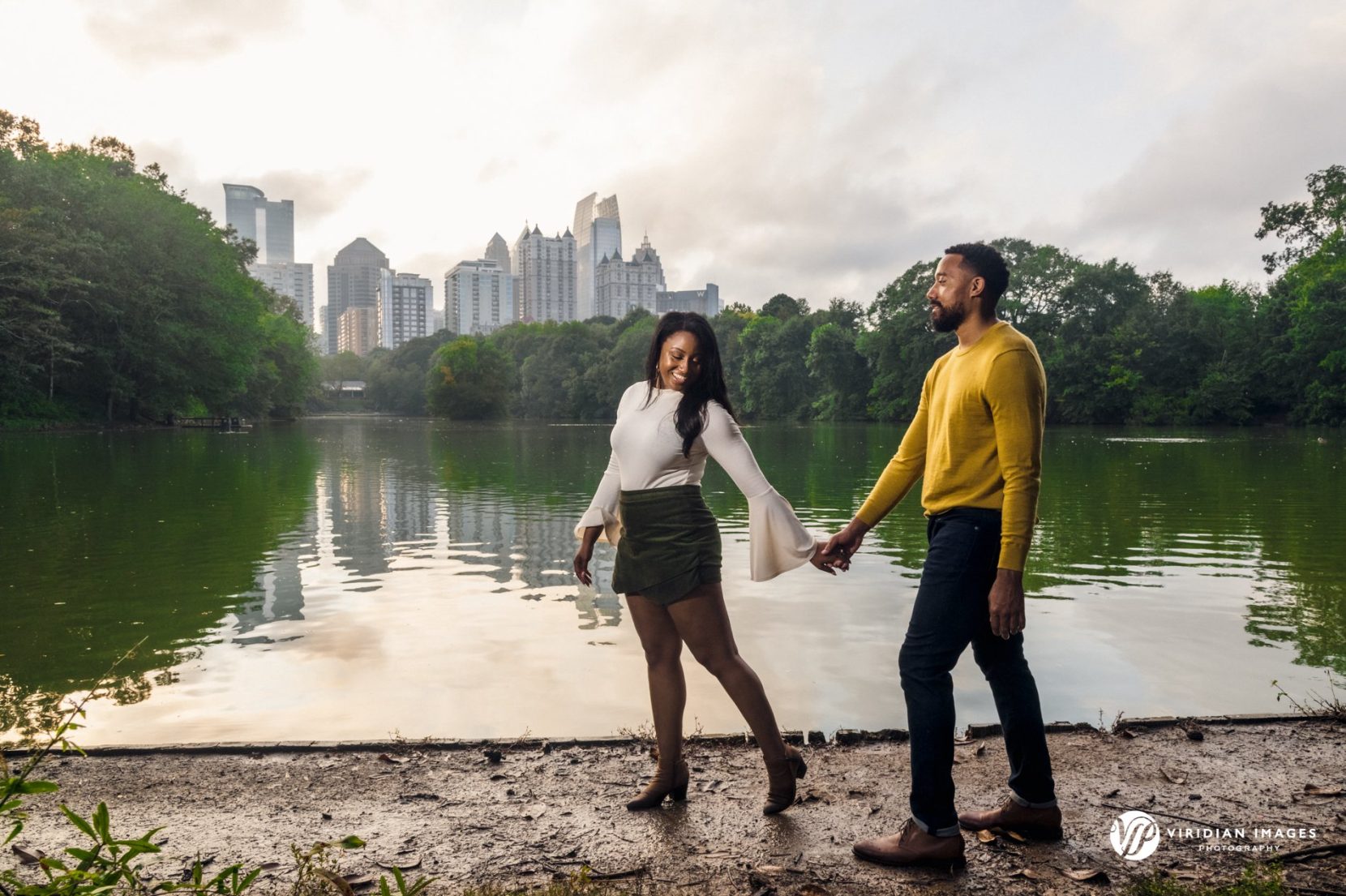 couple walking hand in hand along lake with city skyline reflected on water