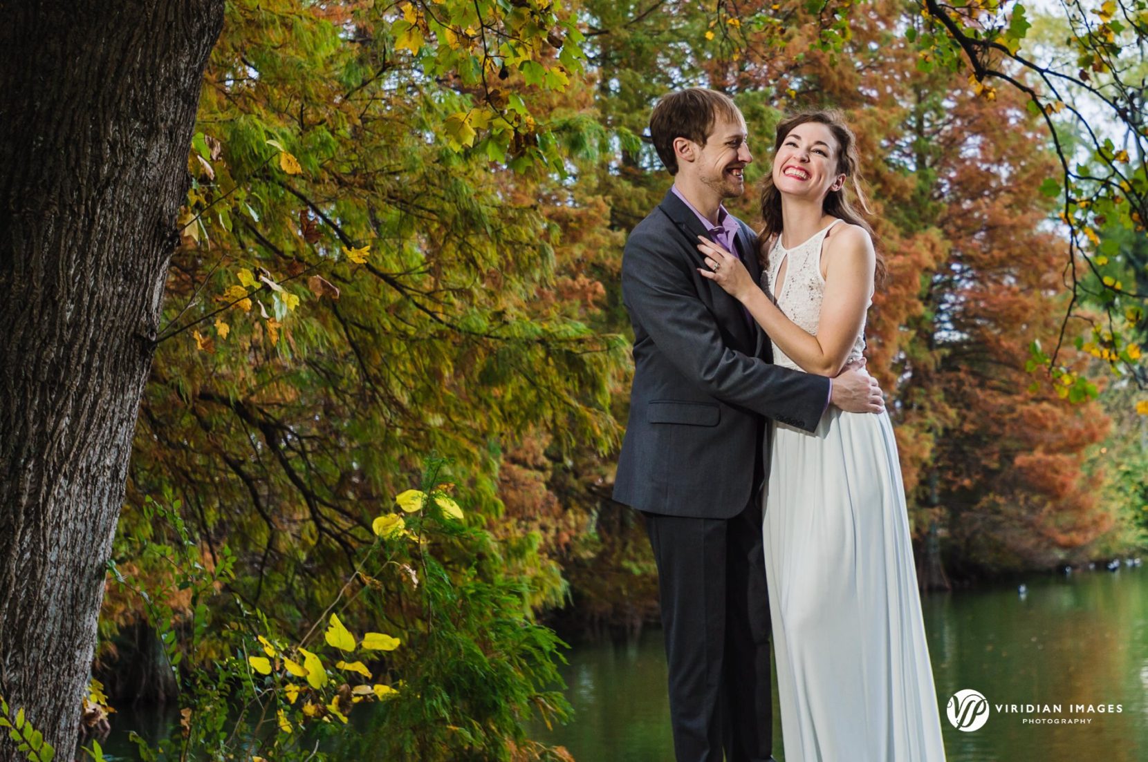 couple laughing along lake during fall engagement session at Piedmont Park
