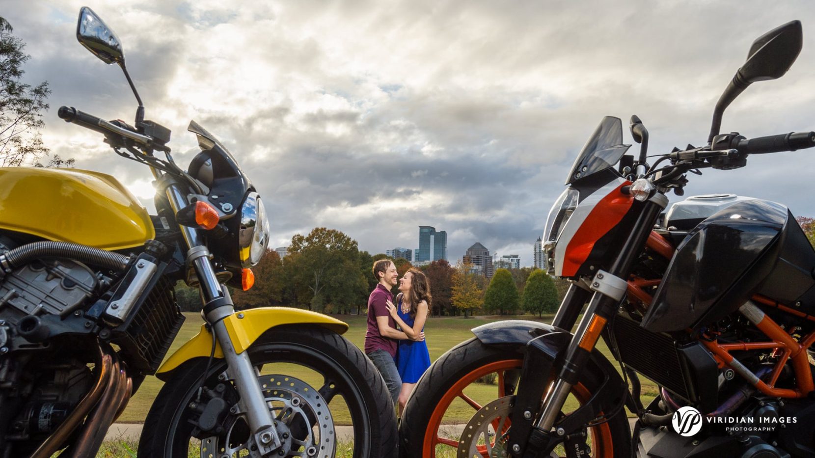 Jenny and James embrace in background against moody skies with motorcycles in the foreground