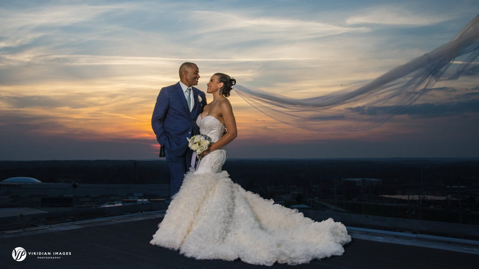 bride with flowy veil and groom on top of Ventanas Atlanta rooftop helipad during golden hour portraits