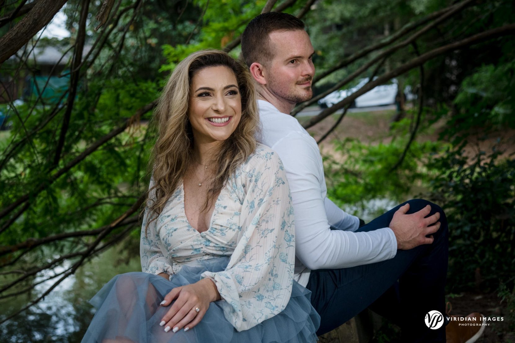 couple sitting back to back on down tree under canopy during drizzling rain