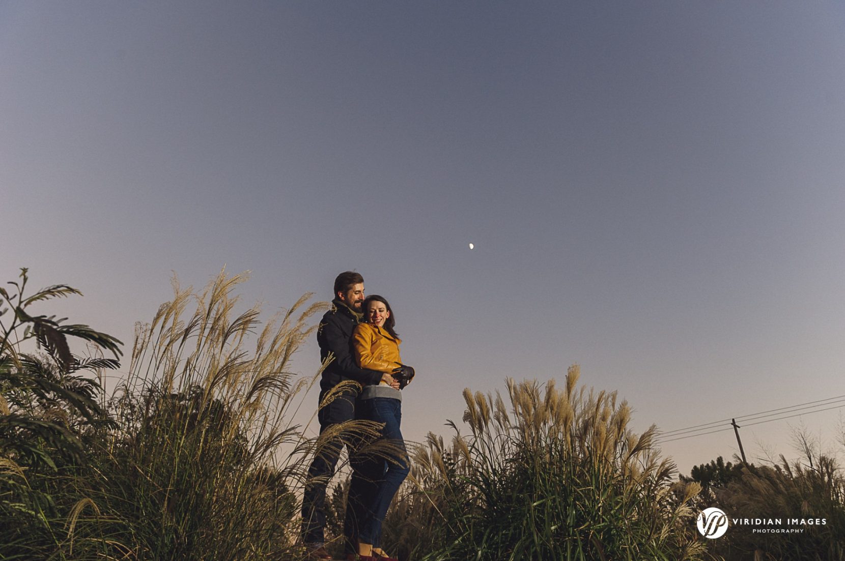 Moody evening engagement portrait with the couple embracing under soft fall light at sunset.