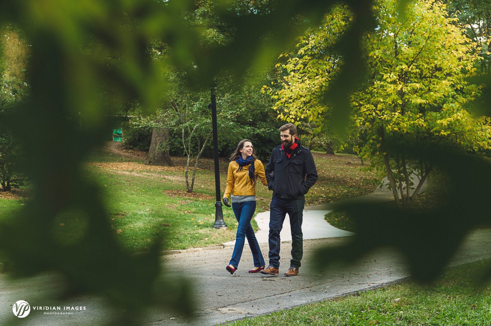 Krista and Zach walking along a tree-lined path during their chilly fall engagement session at Grant Park in Atlanta