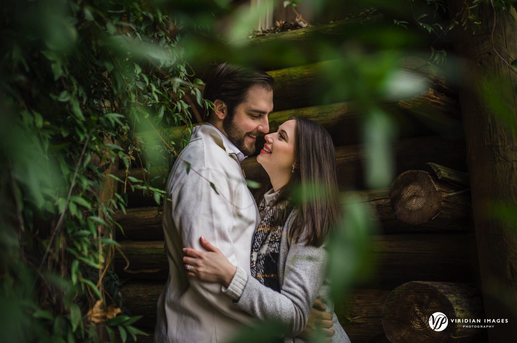 Romantic moment of couple photographed through leaves during winter engagement session at Rocky Lake Estate.