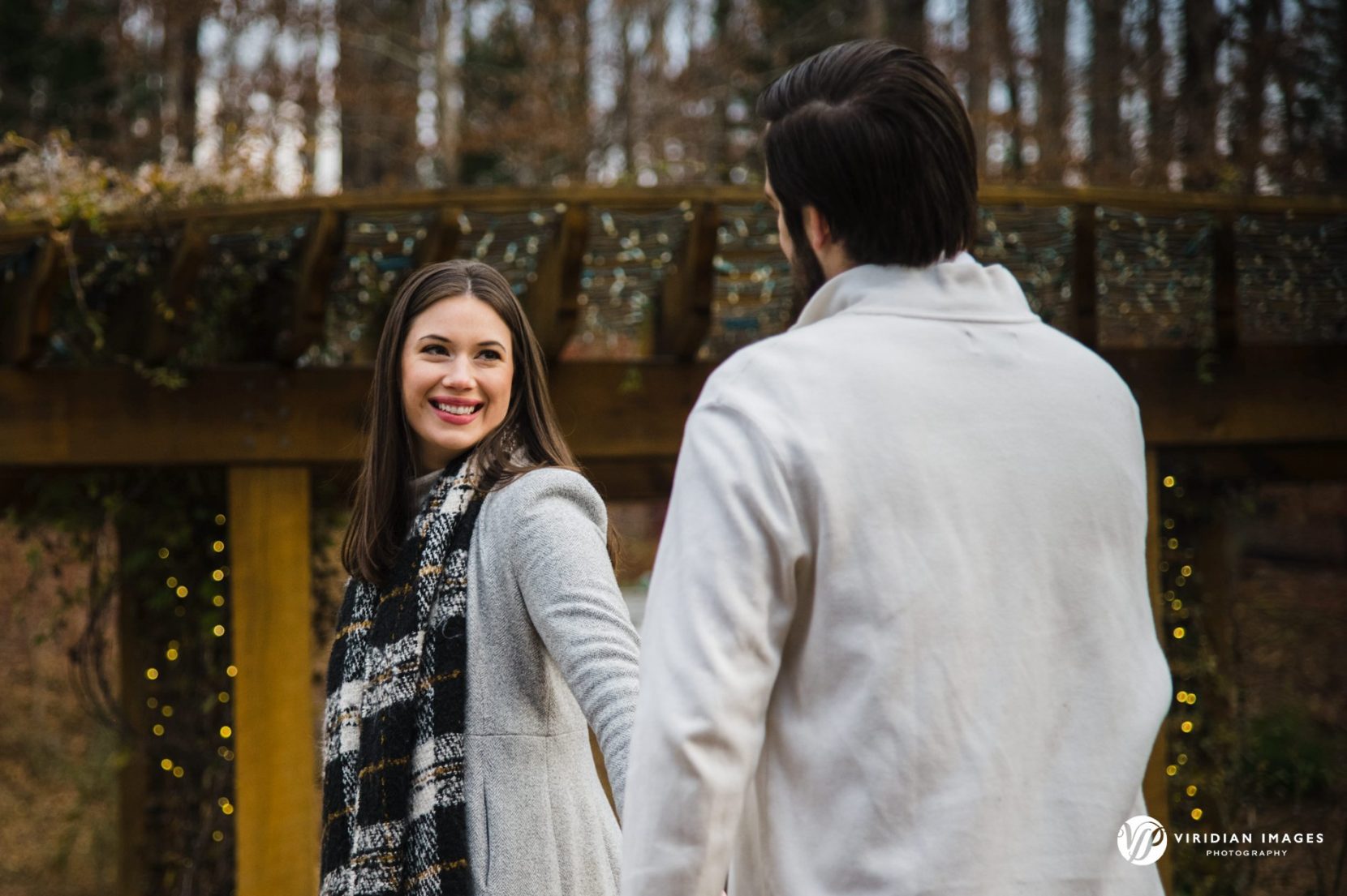 Bride to be looking back on wooden bridge during their winter engagement session.