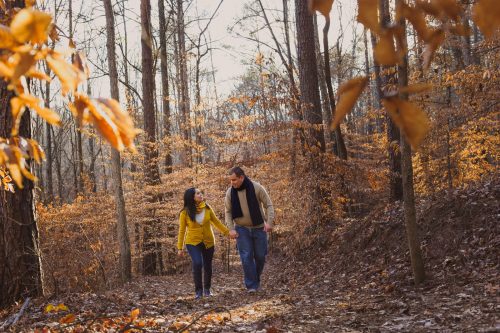 Couple walking together through bare tree trail during their winter engagement session at Sope Creek Trail